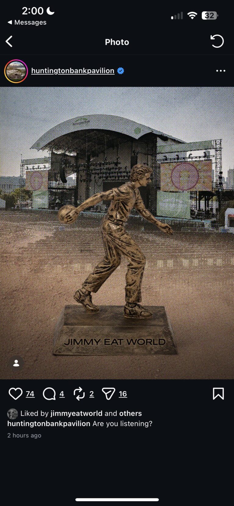 Screenshot of an Instagram post by Huntington Bank Pavilion showing a bronze statue of a person mid-throw holding a ball on a pedestal labeled "JIMMY EAT WORLD" placed in front of an empty outdoor concert stage. The post caption reads "Are you listening?" and the screenshot shows it was liked by jimmyeatworld.