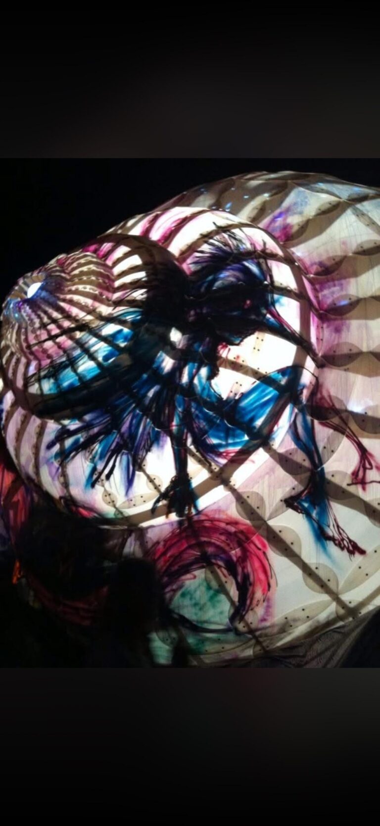 Spherical festival art installation lit from within and covered in projected swirls of blue, pink, and black ink-like patterns that create layered organic shapes and shadowed lattice patterns against a dark background.