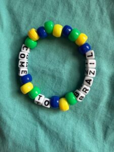 Circular kandi bracelet made from glossy green, yellow, and blue barrel beads and white letter cubes threaded on elastic, with the letter cubes arranged to spell a short message.