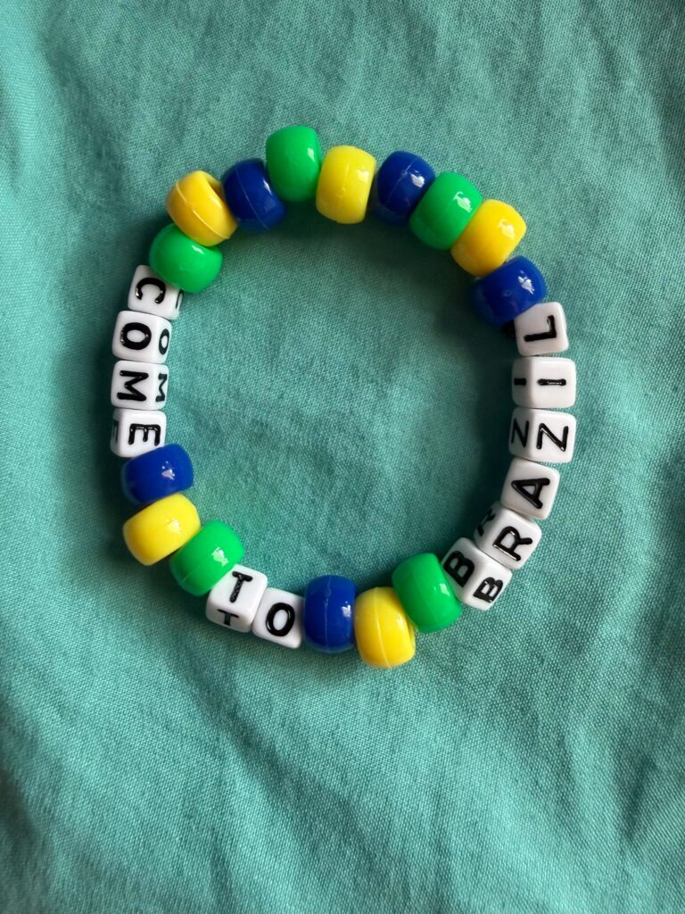 Circular kandi bracelet made from glossy green, yellow, and blue barrel beads and white letter cubes threaded on elastic, with the letter cubes arranged to spell a short message.